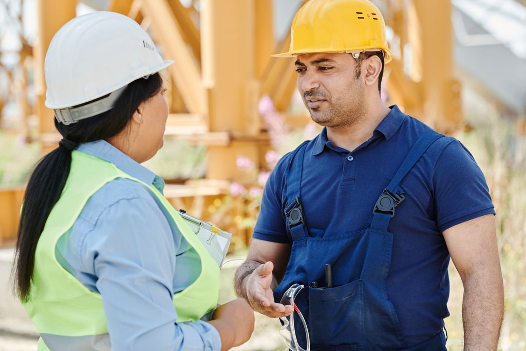 Male and female construction workers discussing safety on a sunny day outdoors.